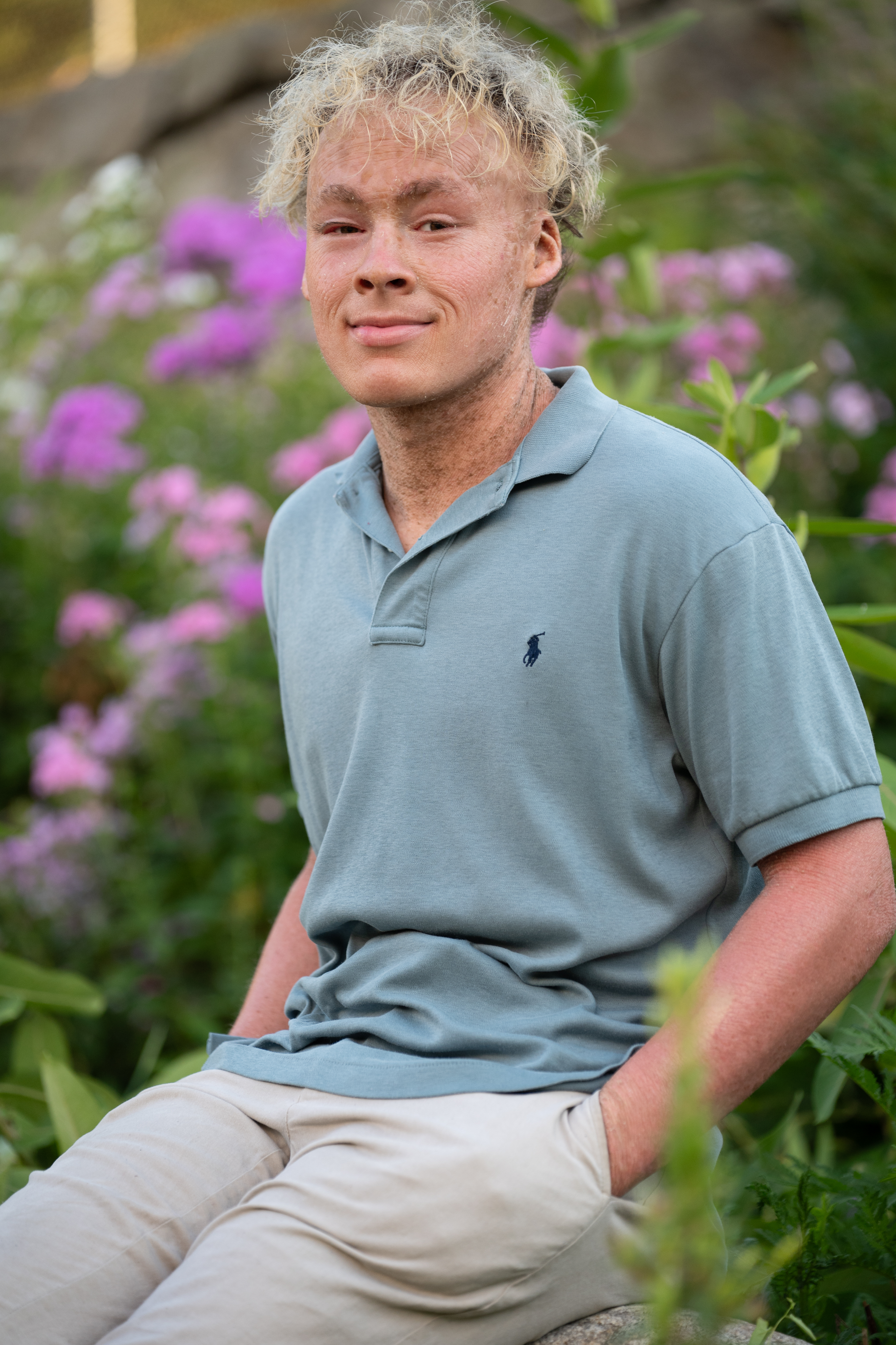 Smiling high school senior in a green polo surrounded by purple flowers