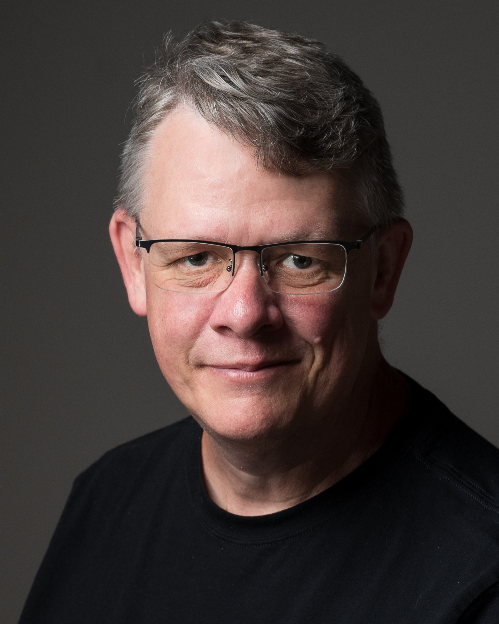 Professional headshot of a man in glasses against a dark background