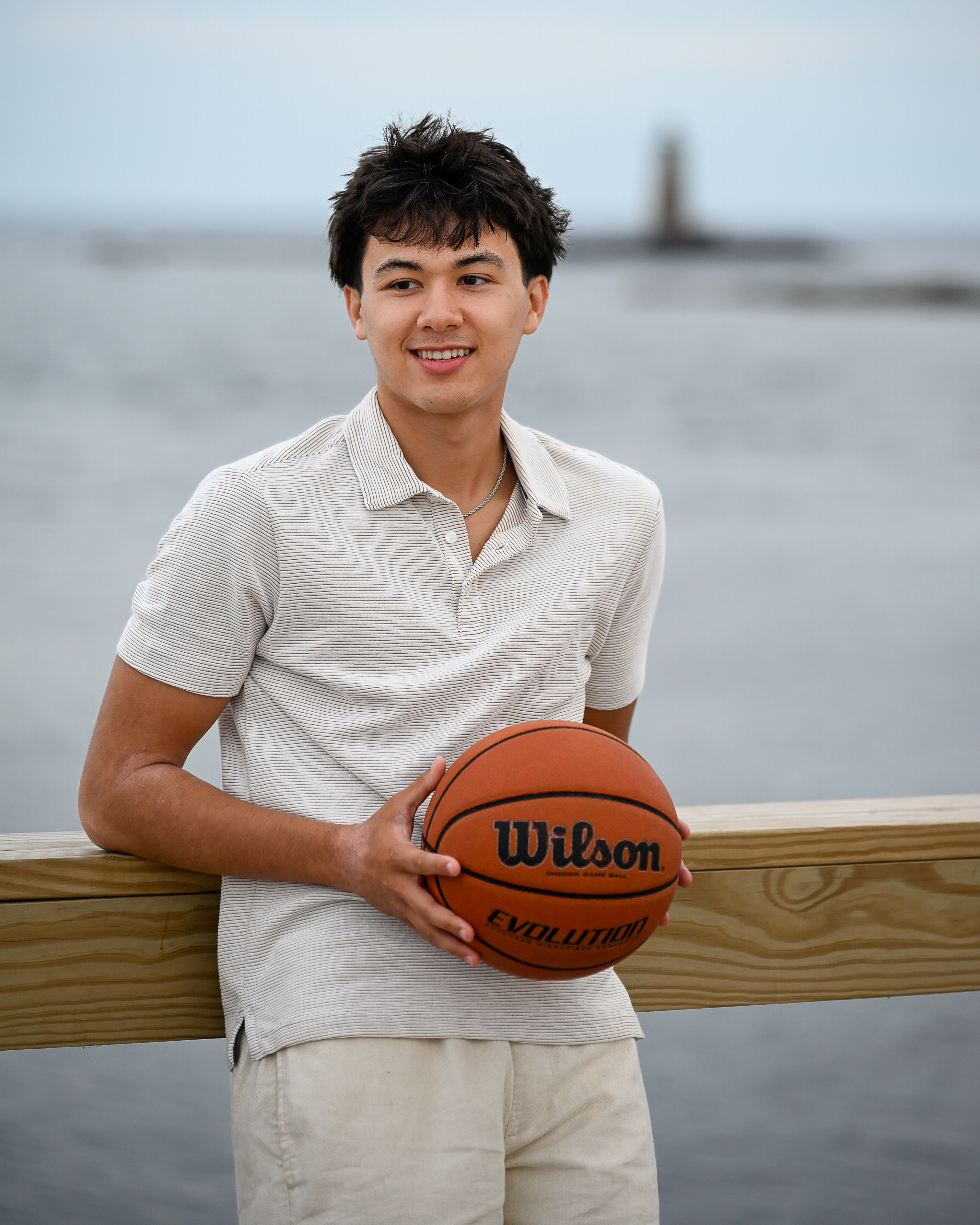 Senior portrait holding a basketball on the pier railing at Fort Foster