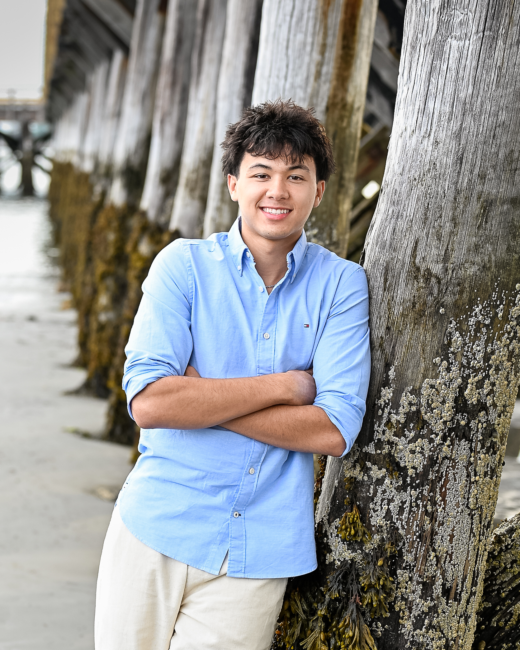 Senior portrait leaning against weathered pier pilings at Fort Foster