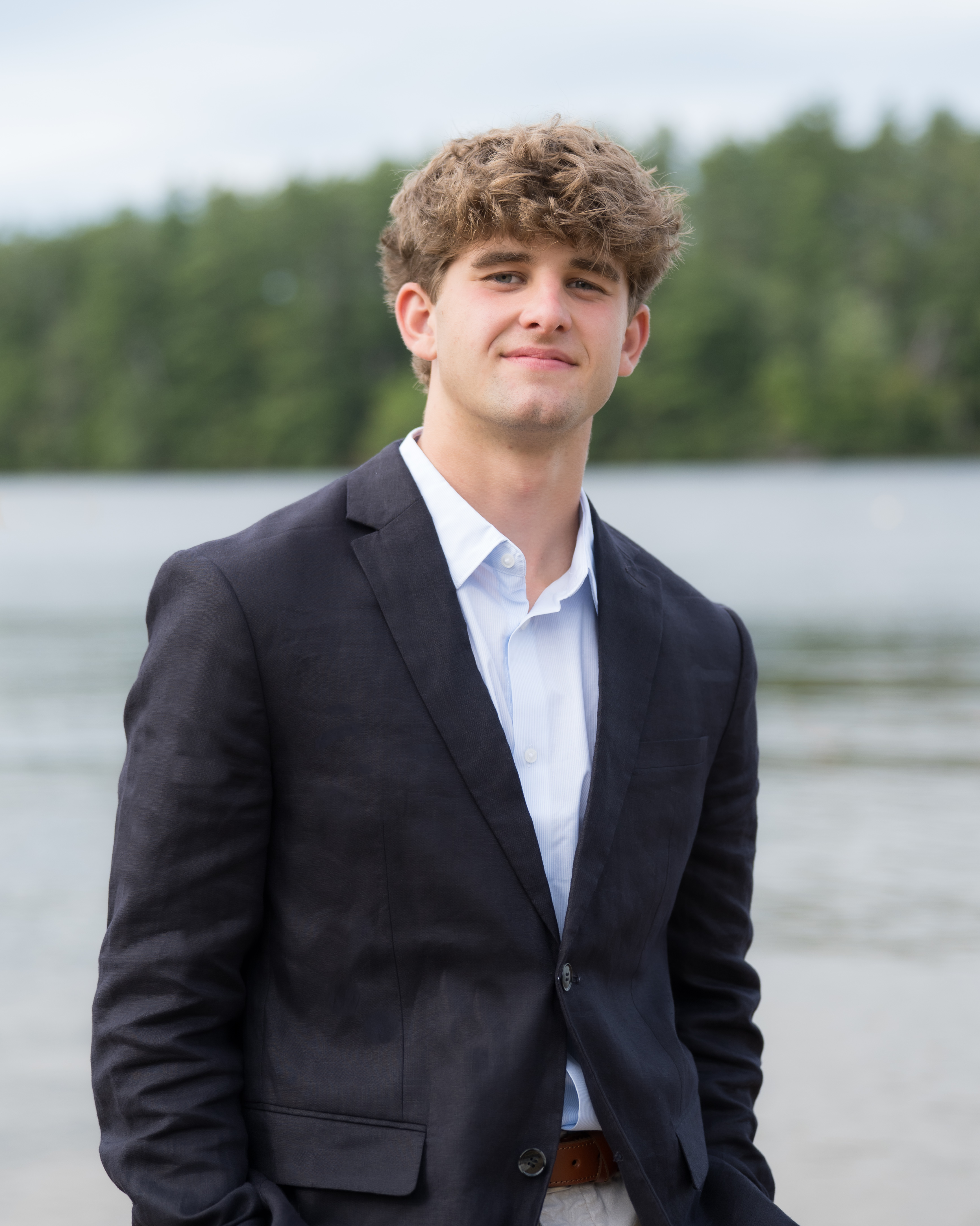 High school senior in a navy blazer and light blue shirt standing by a lake, New Hampshire senior portrait